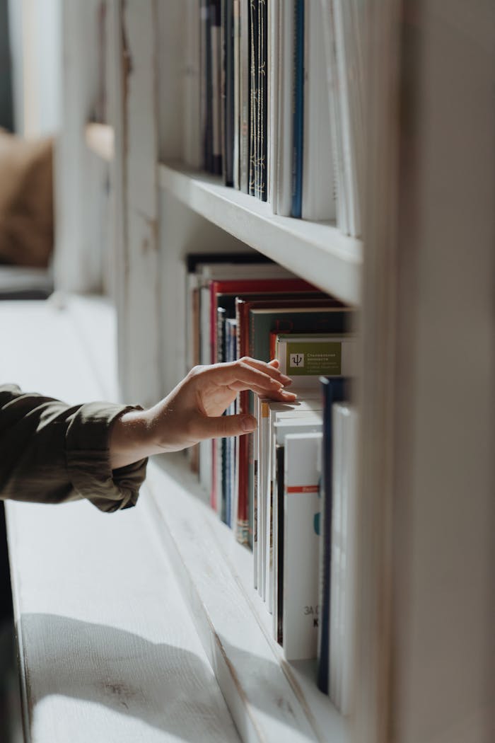 services-01 A hand reaches out to select a book from a well-arranged indoor bookshelf.